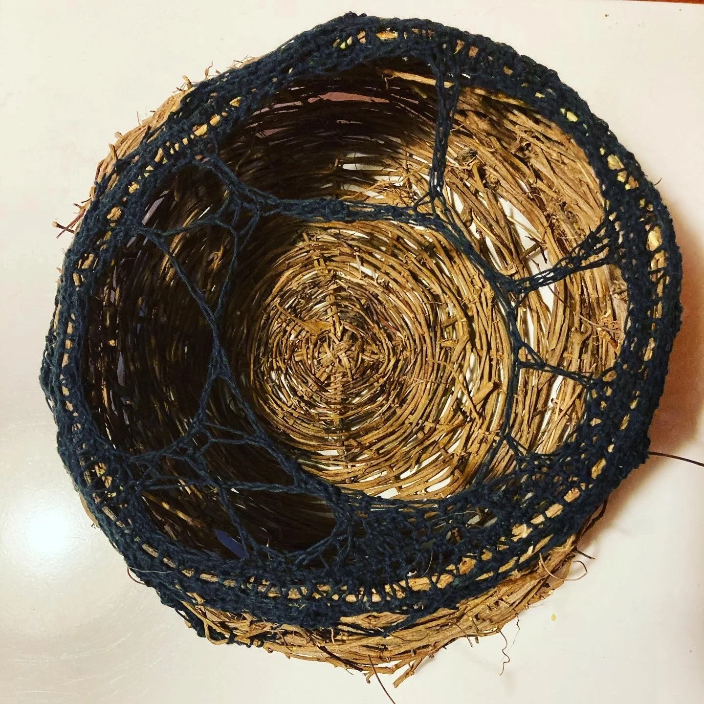 Woven wicker basket with black rope rim, viewed from above.