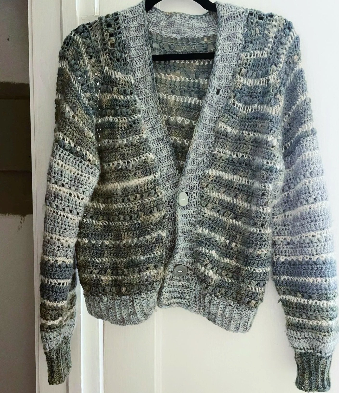 A knitted gray and black striped cardigan hanging on a black hanger.