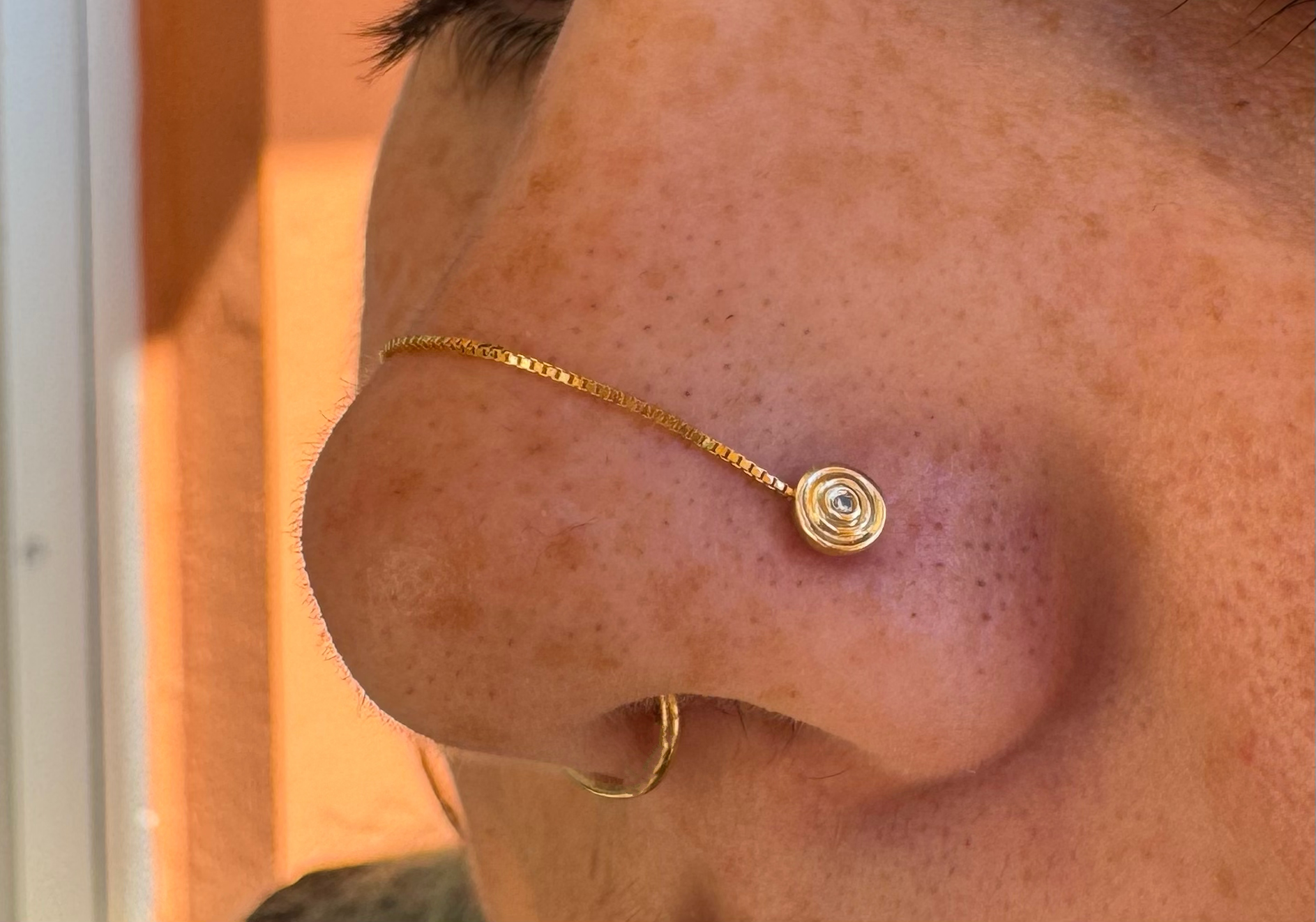 Healed nostril piercing with a yellow gold impulse end from Ember Jewelry with a genuine white diamond and a box chain from Buddha Jewelry