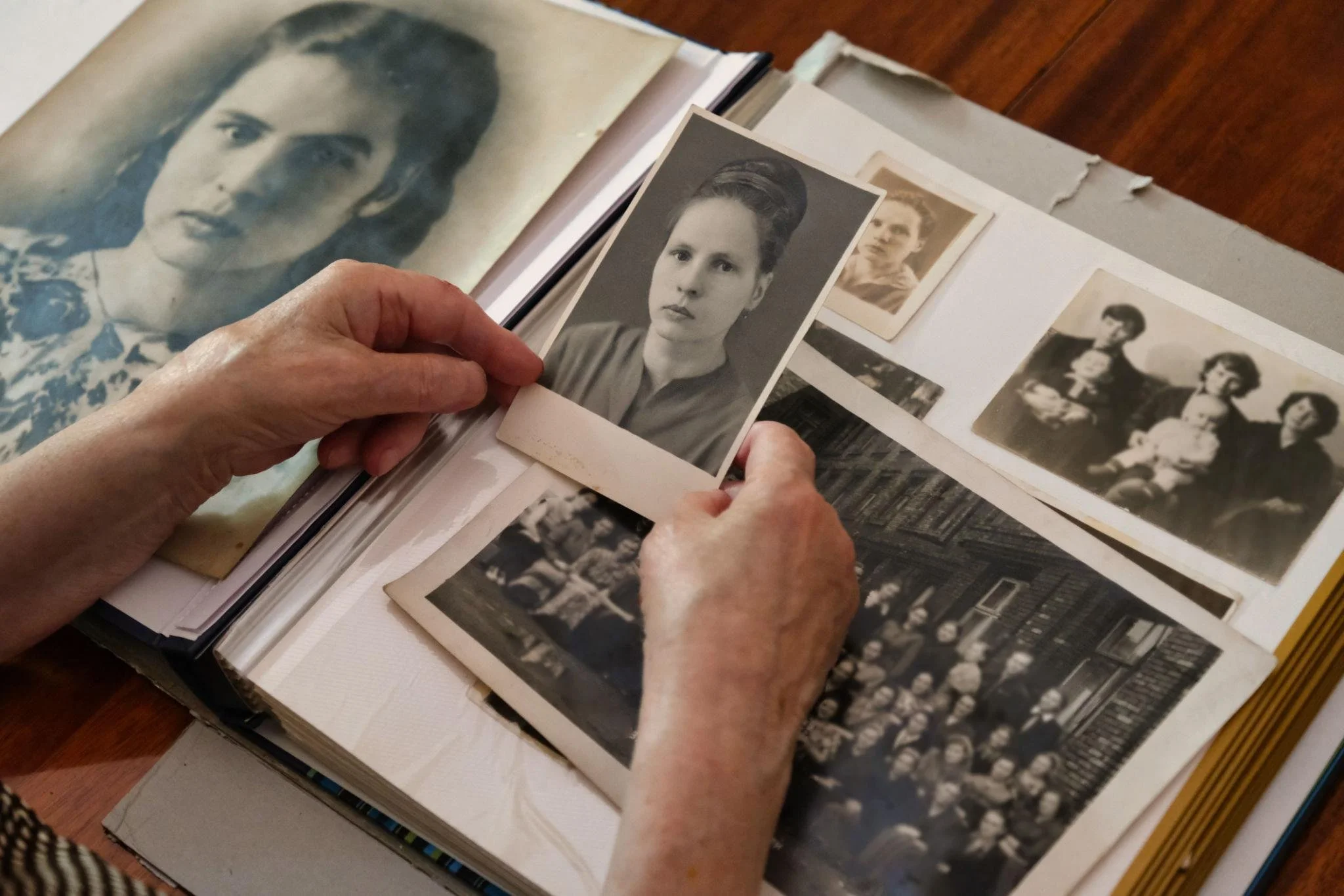 Person holding black-and-white portrait photographs of a woman and a man, with other old photographs visible on a table.