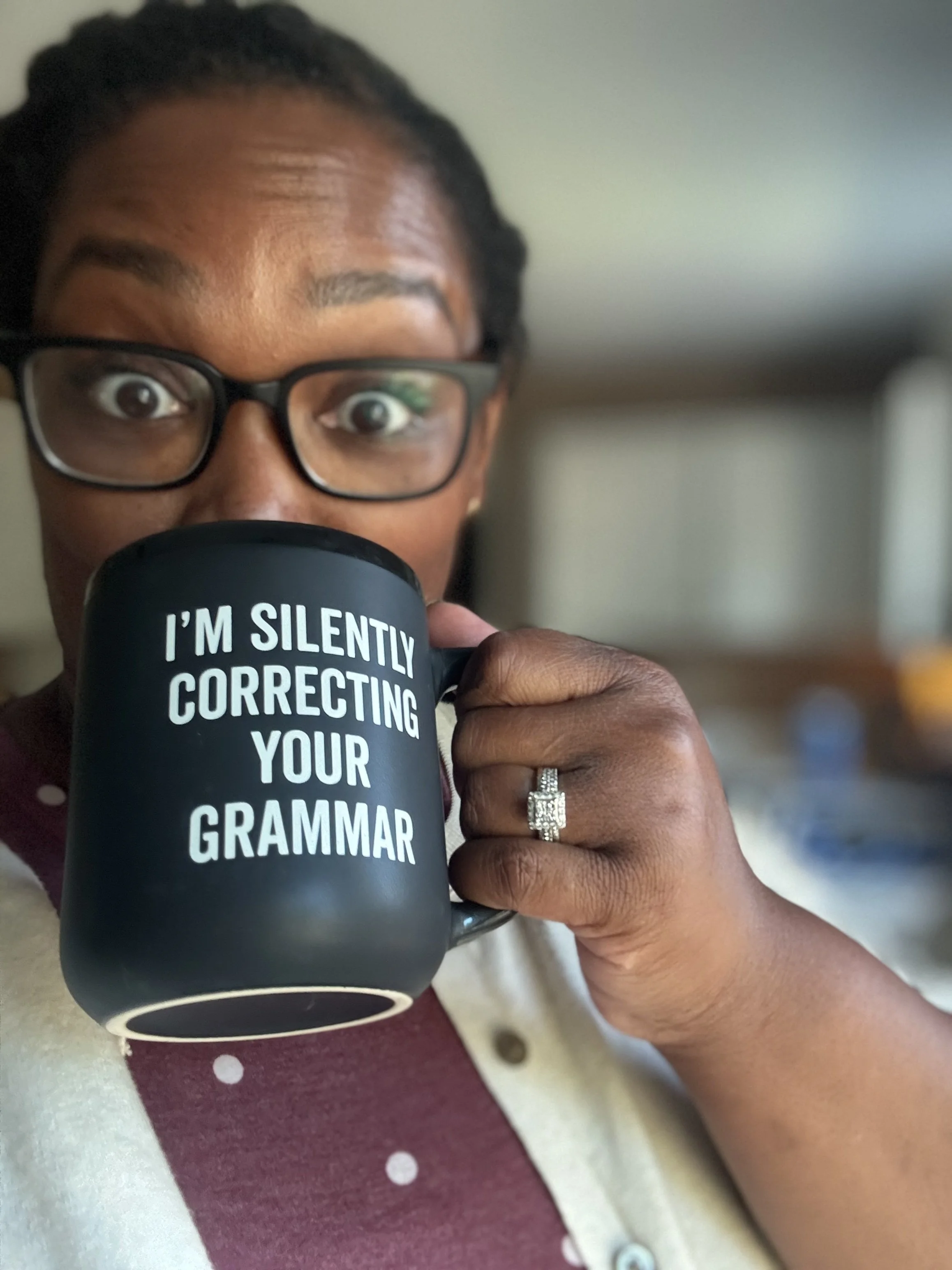 A person with glasses holding a black mug that says, "I'm silently correcting your grammar."