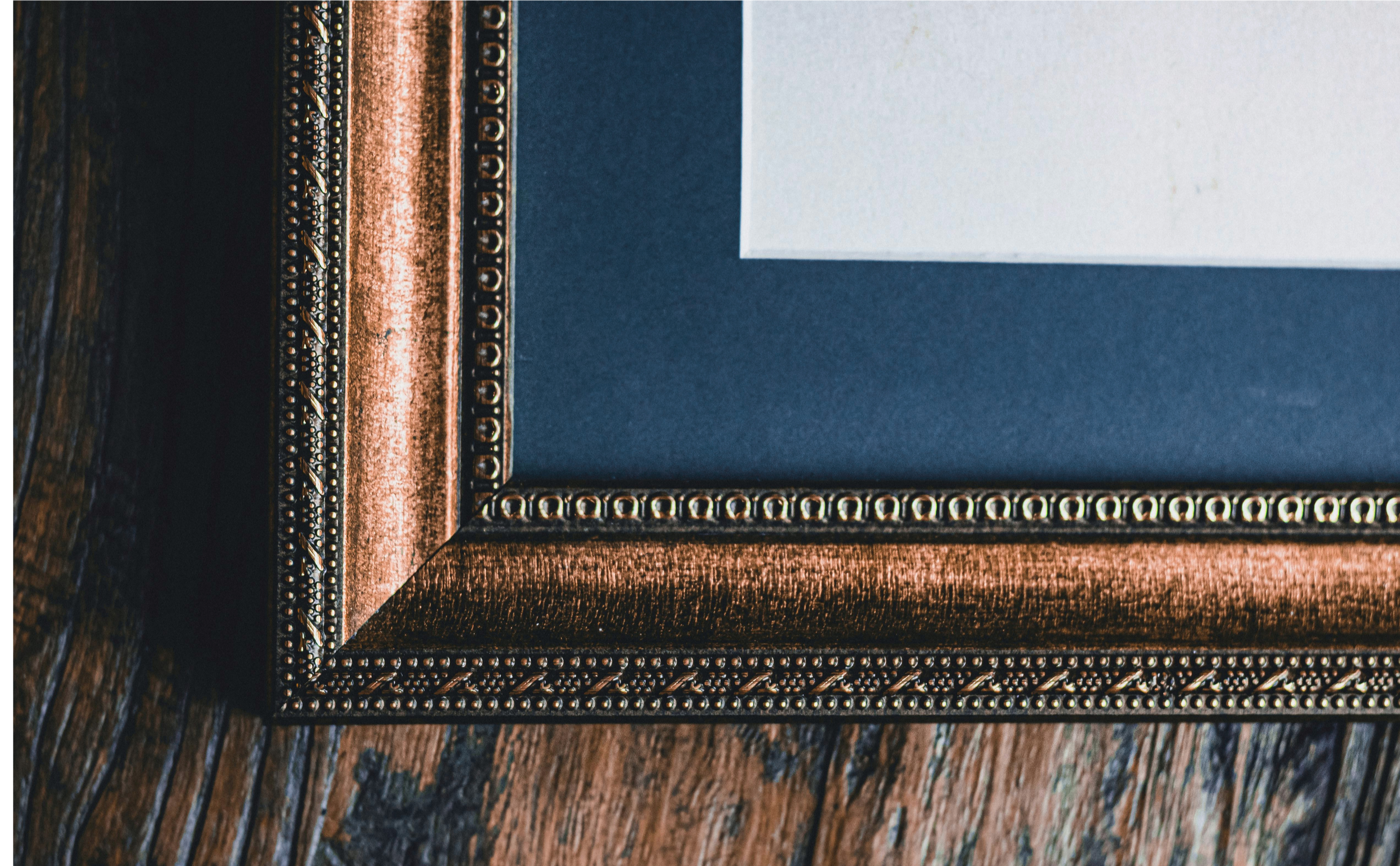 Close-up of a decorative picture frame with intricate beaded and woven metal designs, resting on a wooden surface.
