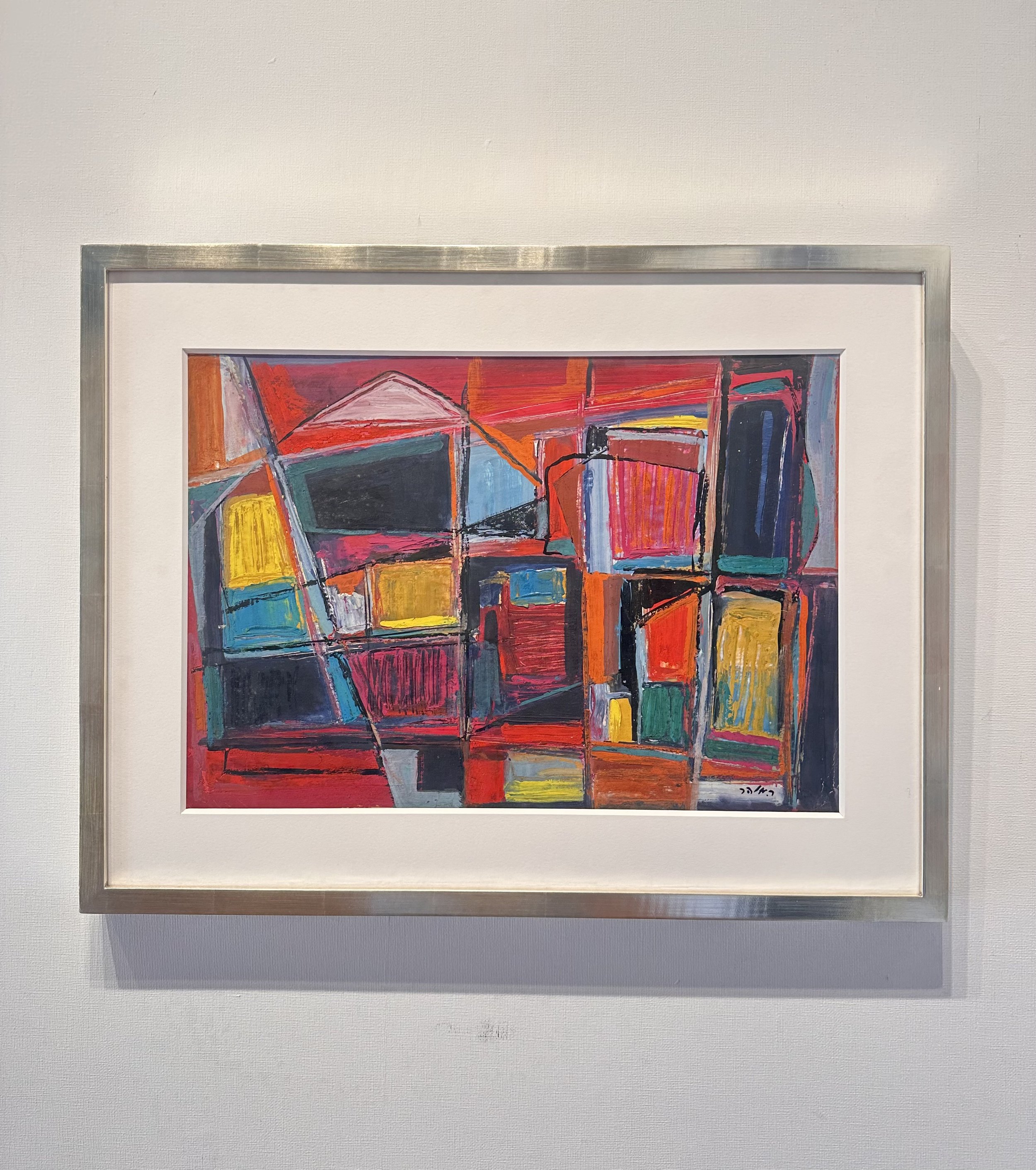 Abstract colorful painting with red, orange, yellow, blue, black, and pink geometric shapes framed in silver, hanging on a white wall.