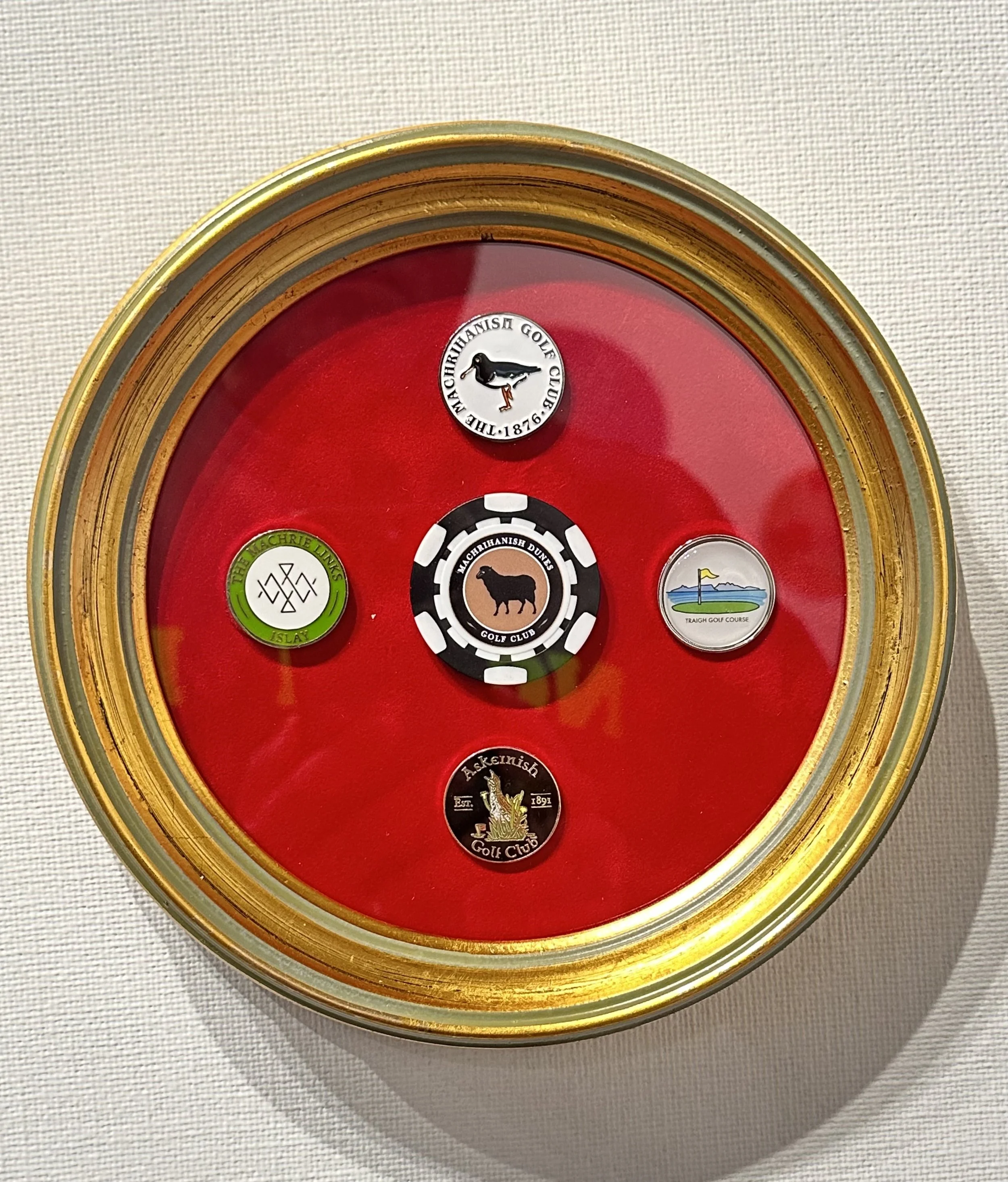 A round shadow box with a red background displaying five golf club badges, including logos and names of various golf clubs.