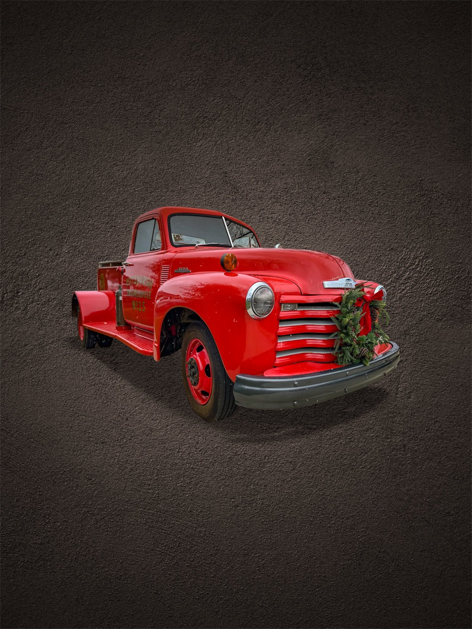 Red vintage fire truck with Christmas greenery and bow on the front, set against a dark background.