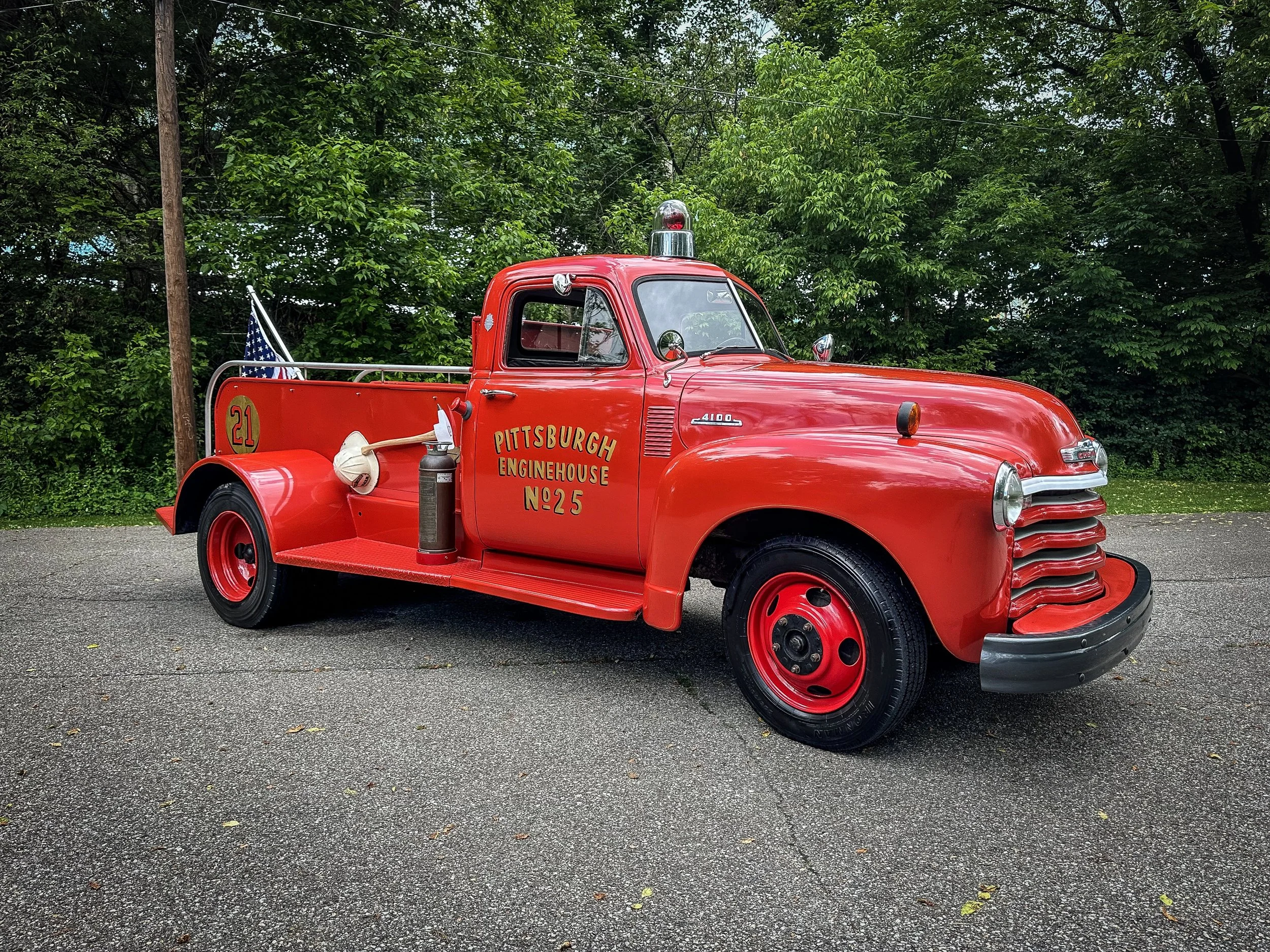 Vintage red fire truck with Christmas decorations on the front, including a pine wreath with a red bow, and the text 'Pittsburgh Enginehouse No. 25' on the door, set against a dark background.