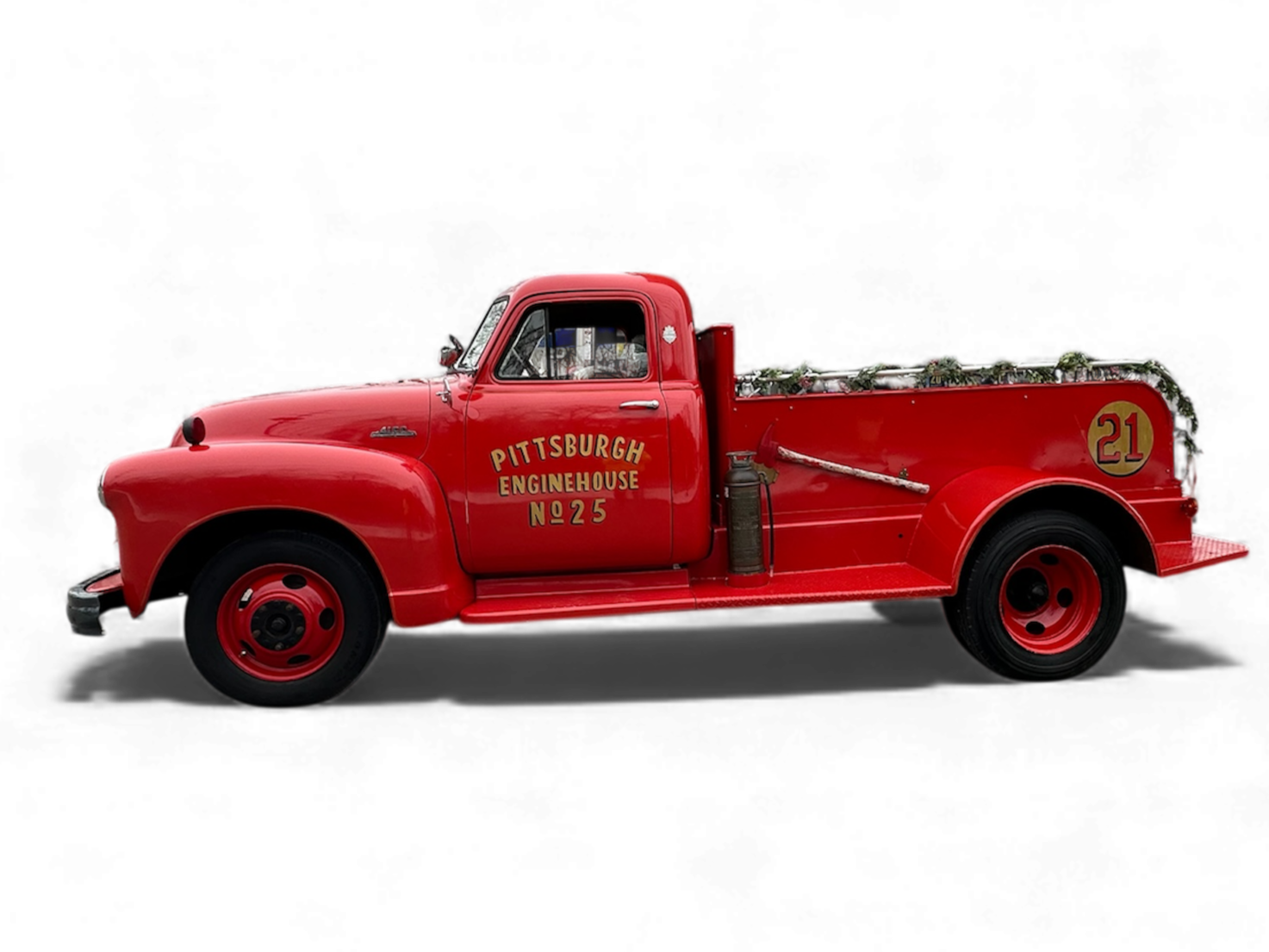 Red vintage fire truck with yellow lettering reading 'Pittsburgh Enginehouse No. 25' and the number 21 on the side, decorated with Christmas garland.