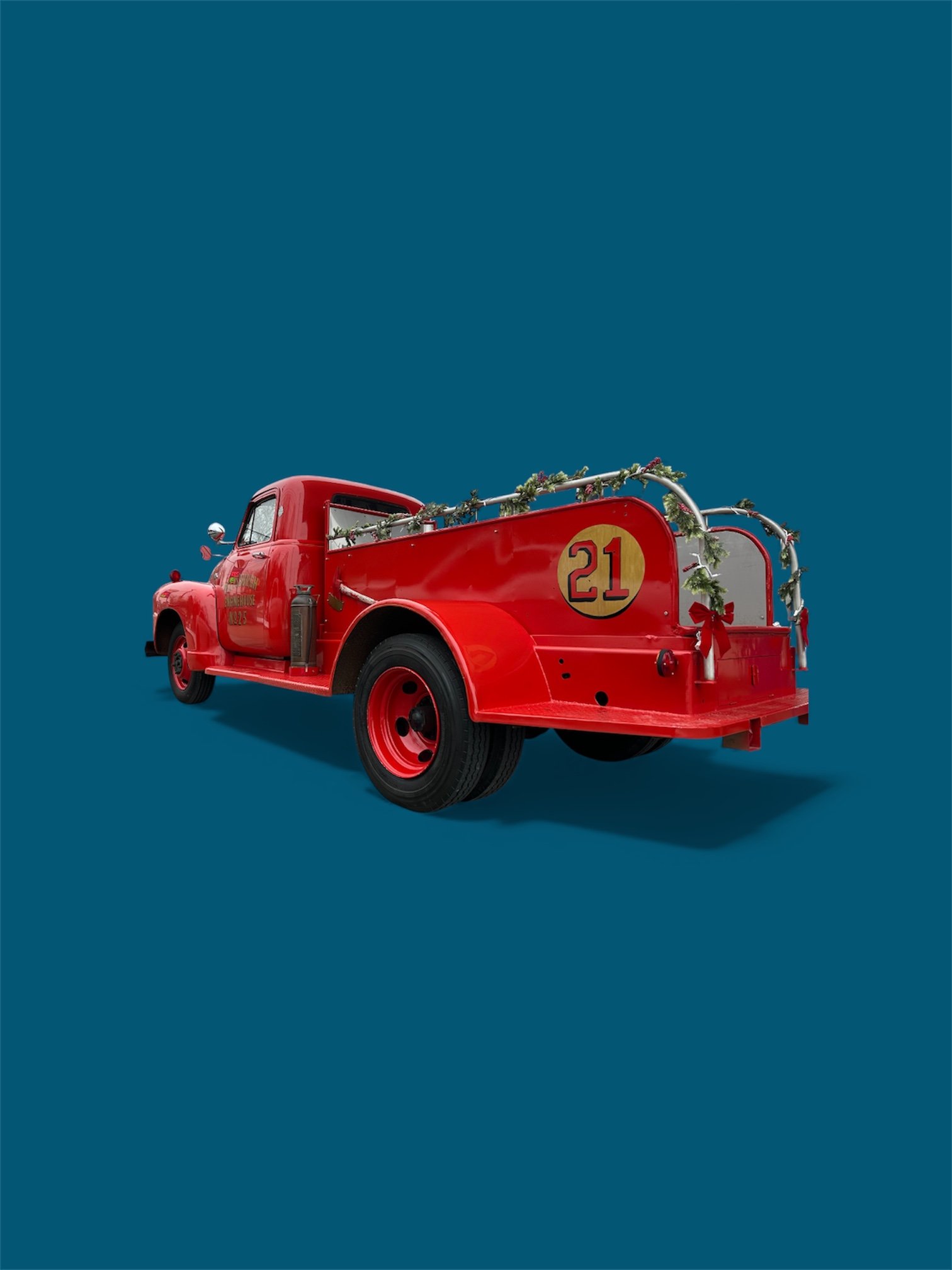 Red vintage fire truck decorated with Christmas garland and a red bow, marked with the number 21, on a blue background.