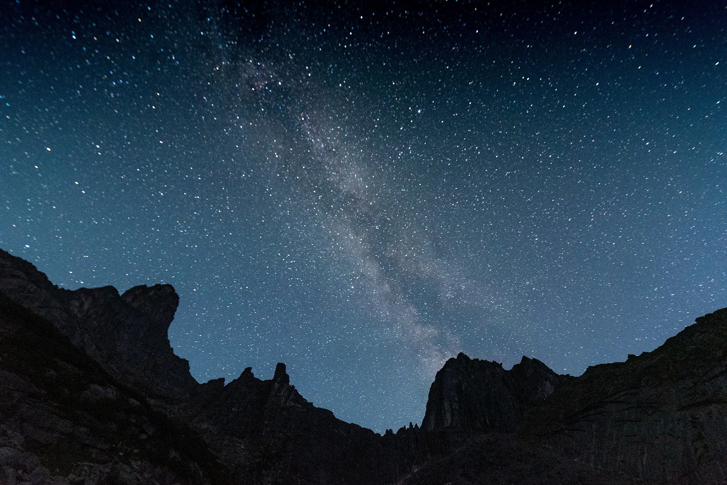 Night sky filled with stars and the Milky Way galaxy, with dark mountain silhouettes in the foreground.