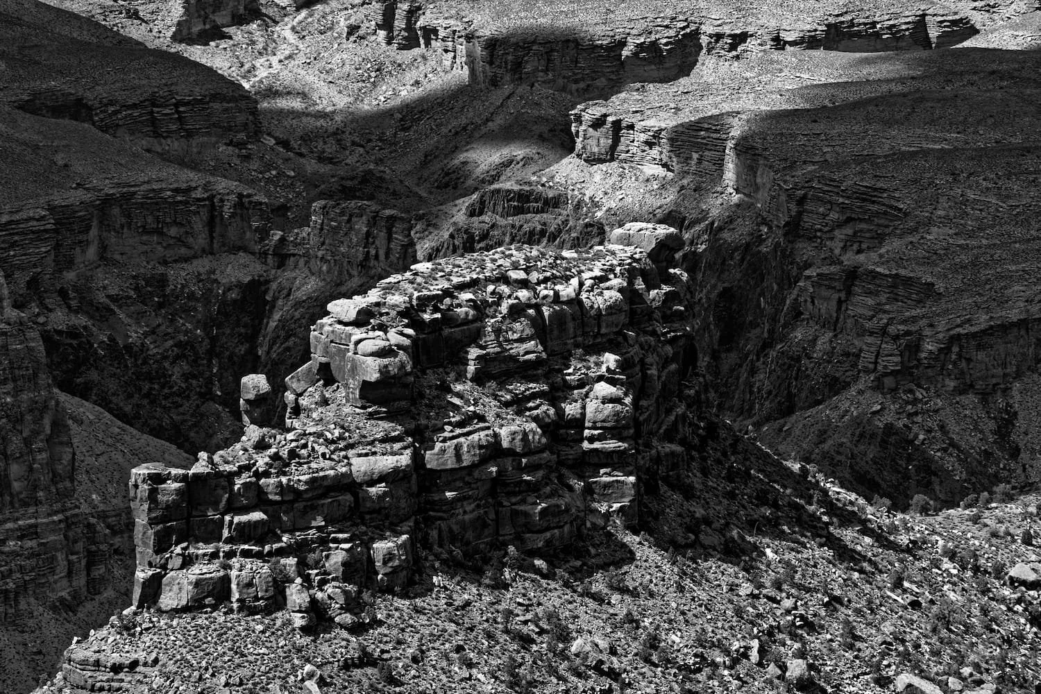Black and white photo of the Grand Canyon with layered rock formations and steep cliffs.