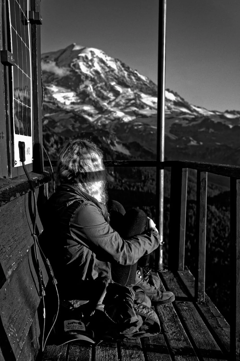 Person sitting on a wooden observation deck, looking at a snow-capped mountain in the distance.