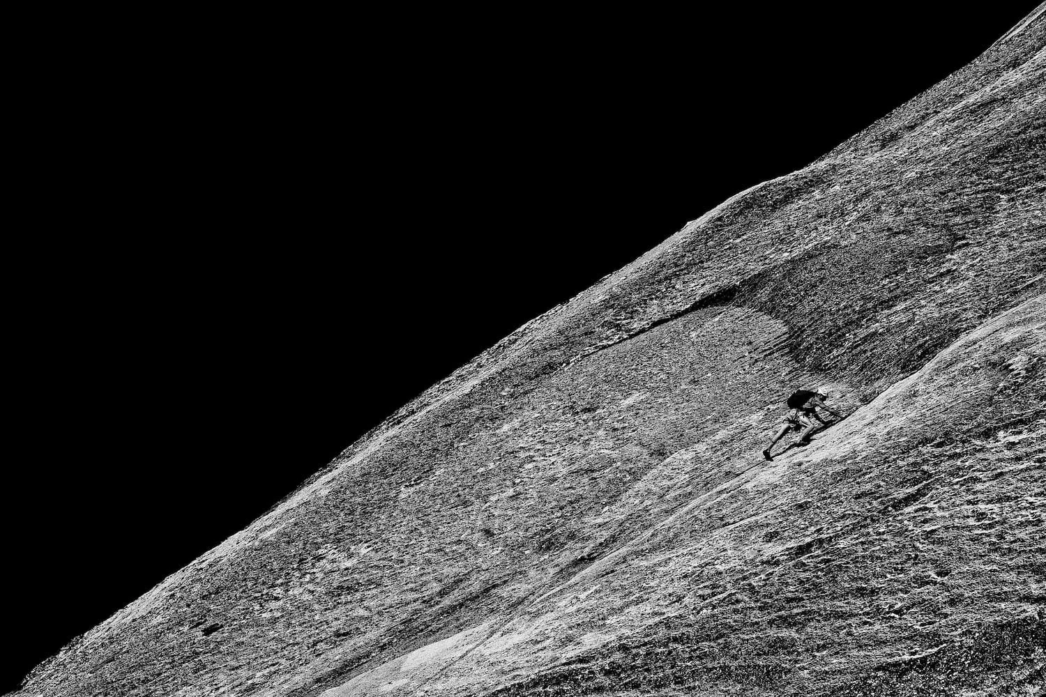 A person rock climbing on a steep, textured surface with a dark sky in the background.