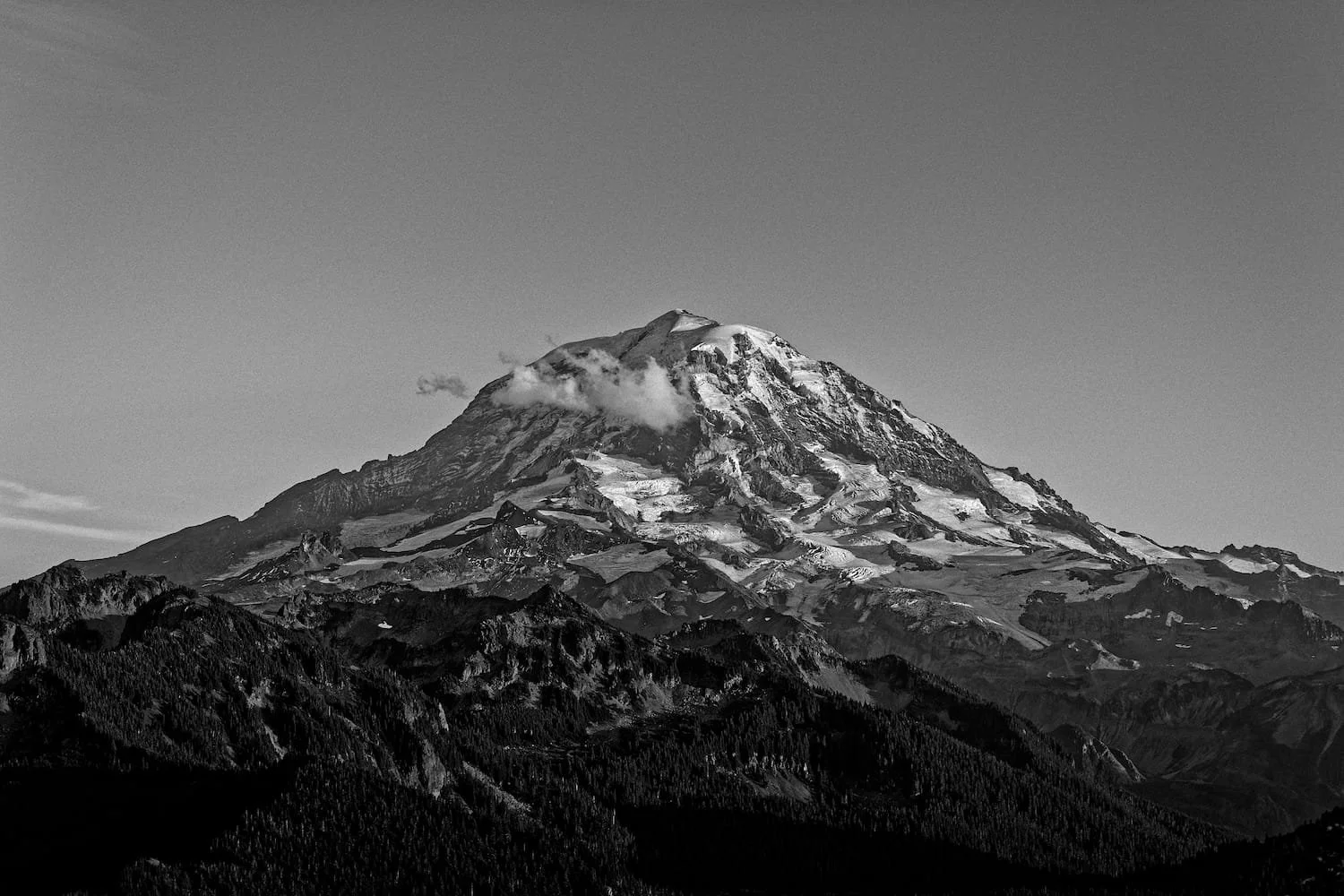 Black and white photograph of a snow-capped mountain with cloudy sky.