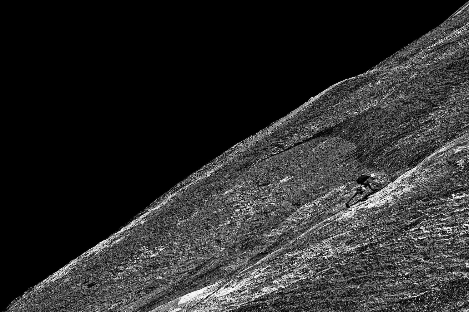 A person climbing a steep, rocky mountain slope with a dark sky in the background.