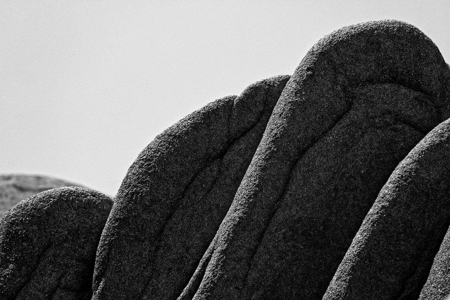 Close-up of large, textured, dark rocks stacked in a formation with a bright sky in the background.