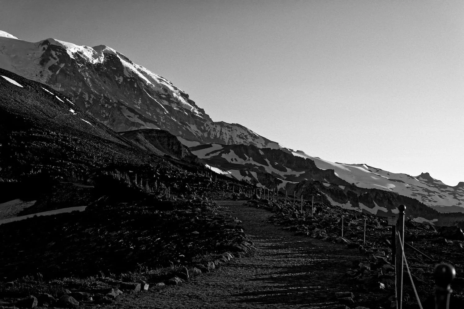Snow-capped mountains with a dirt trail and a rope fence along the path.