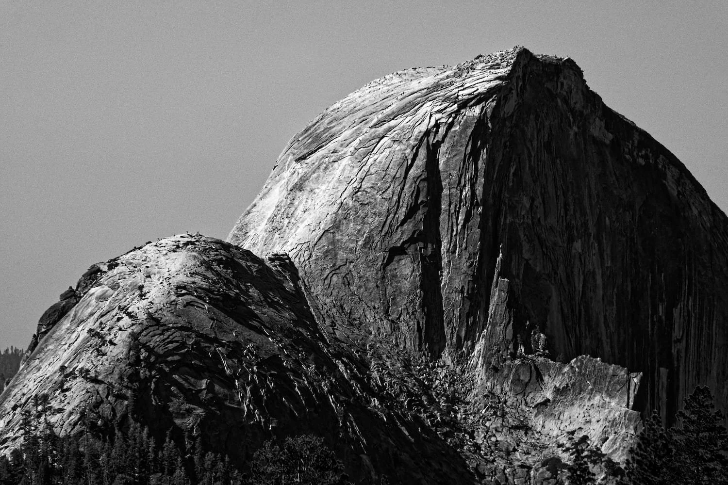 Black and white photo of large rocky mountain formations with textured surfaces and a clear sky above.