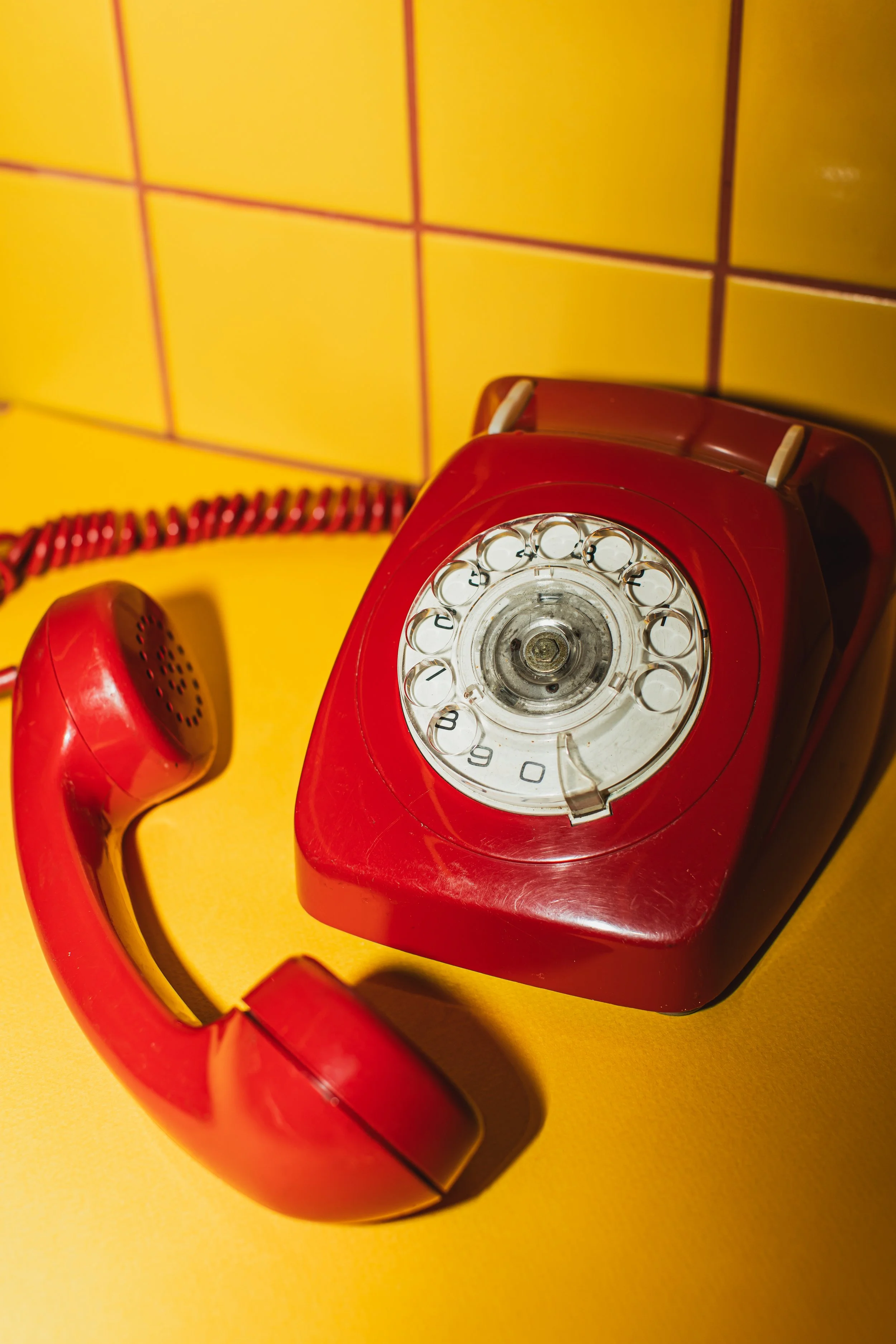 Red rotary dial telephone with a coiled cord on a yellow background.