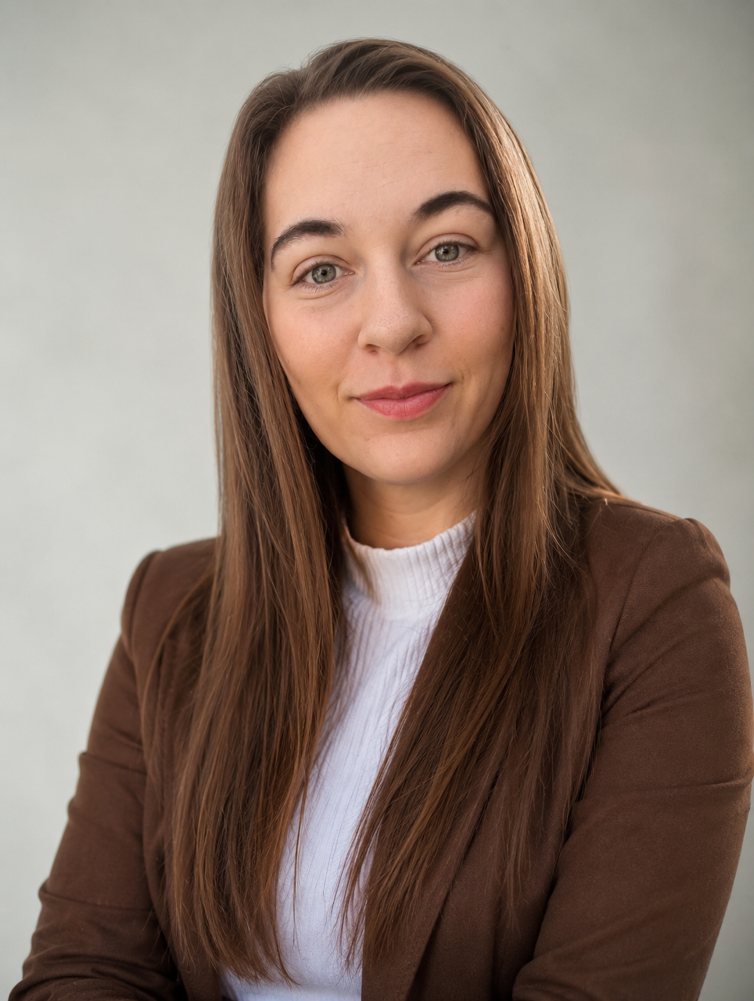 Professional Headshot of Georgina. She has long brown hair, blue eyes, and is Caucasian. Georgina is wearing a brown blazer and a white high collar white shirt.