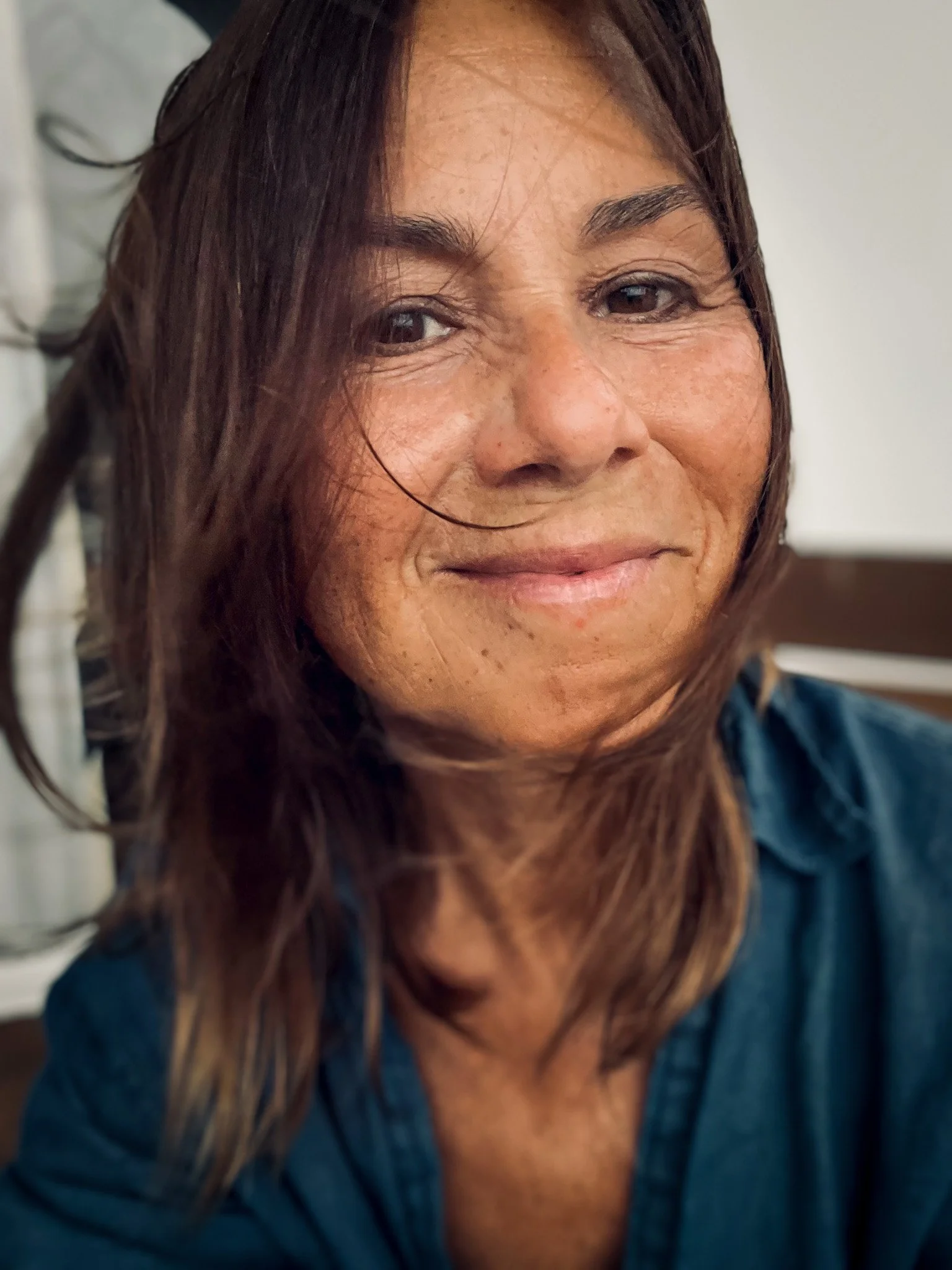 Close-up of a woman with brown hair, smiling, wearing a blue shirt.