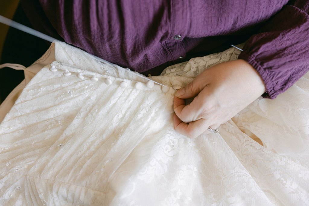 Person sewing a wedding dress with an embroidery pattern using a needle and white thread.