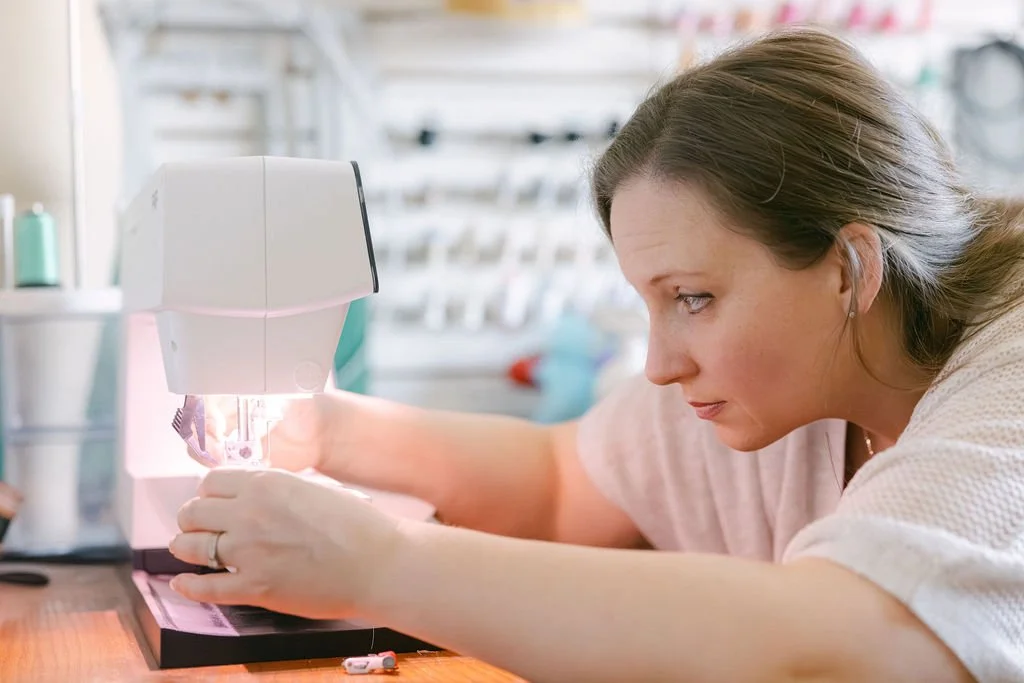 A woman sewing with a sewing machine on a work table in a craft room.
