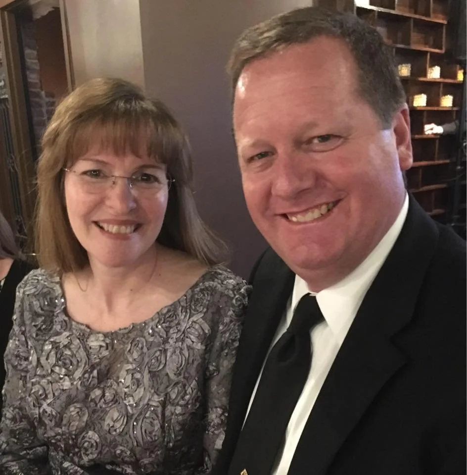 A man and a woman smiling, dressed in formal attire, at a social event.