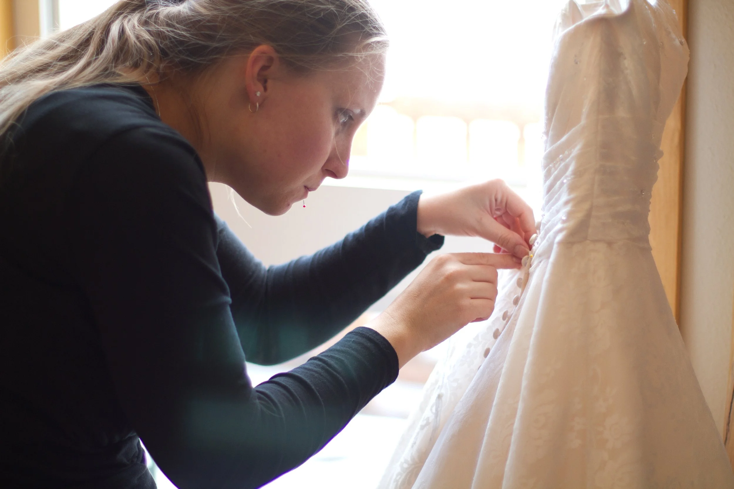 A woman is examining a wedding dress, adjusting the buttons on the back of the dress.