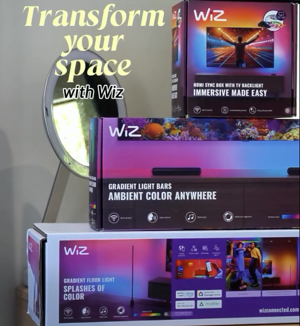 Boxes of WIZ smart lighting products with colorful LED lighting features, placed on a table in front of a mirror, advertising transforming your space with immersive ambient lighting.