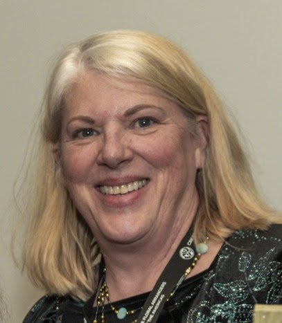Smiling woman with blonde hair wearing a black top and a lanyard.