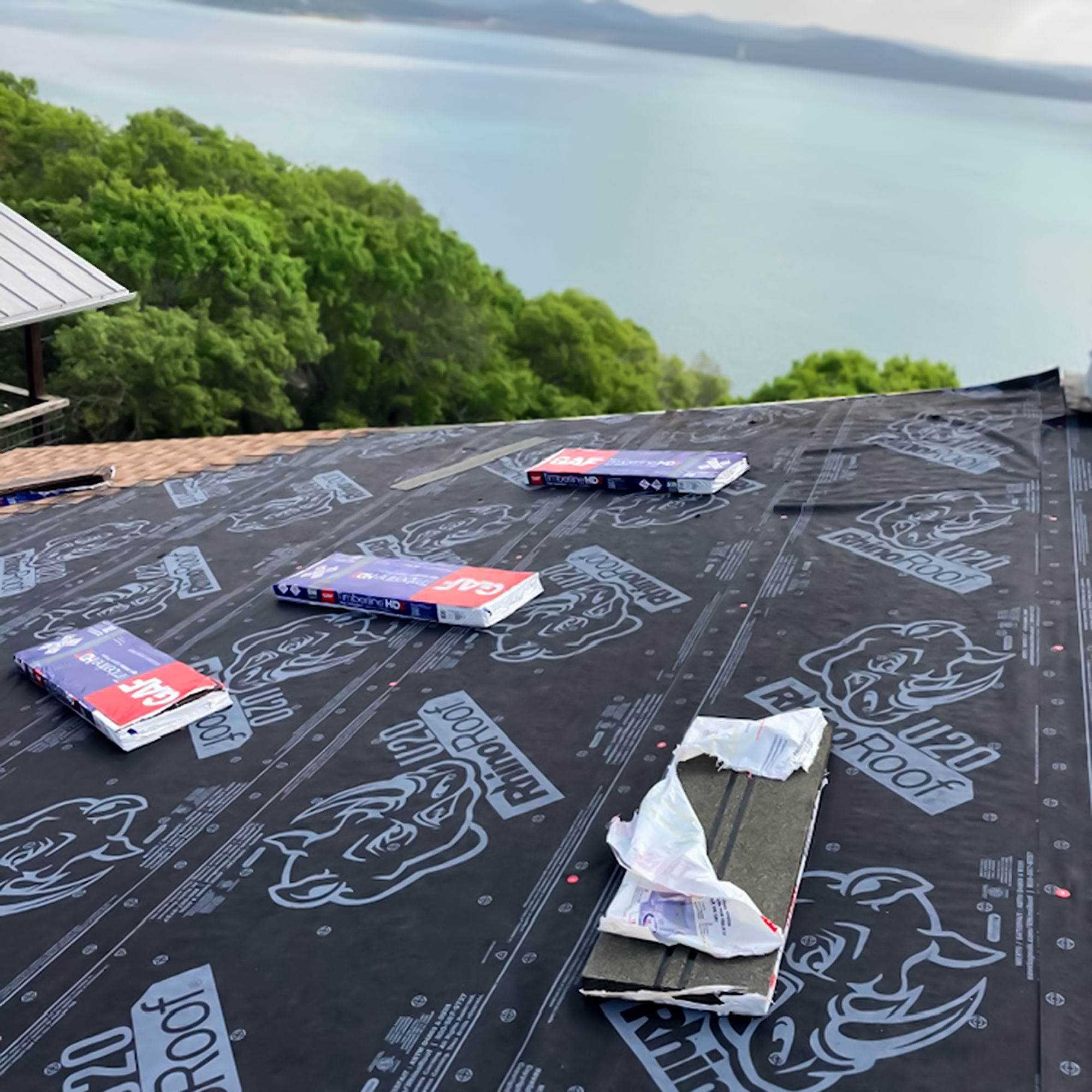 Roof under construction with roofing felt and insulation, overlooking a green landscape and water.