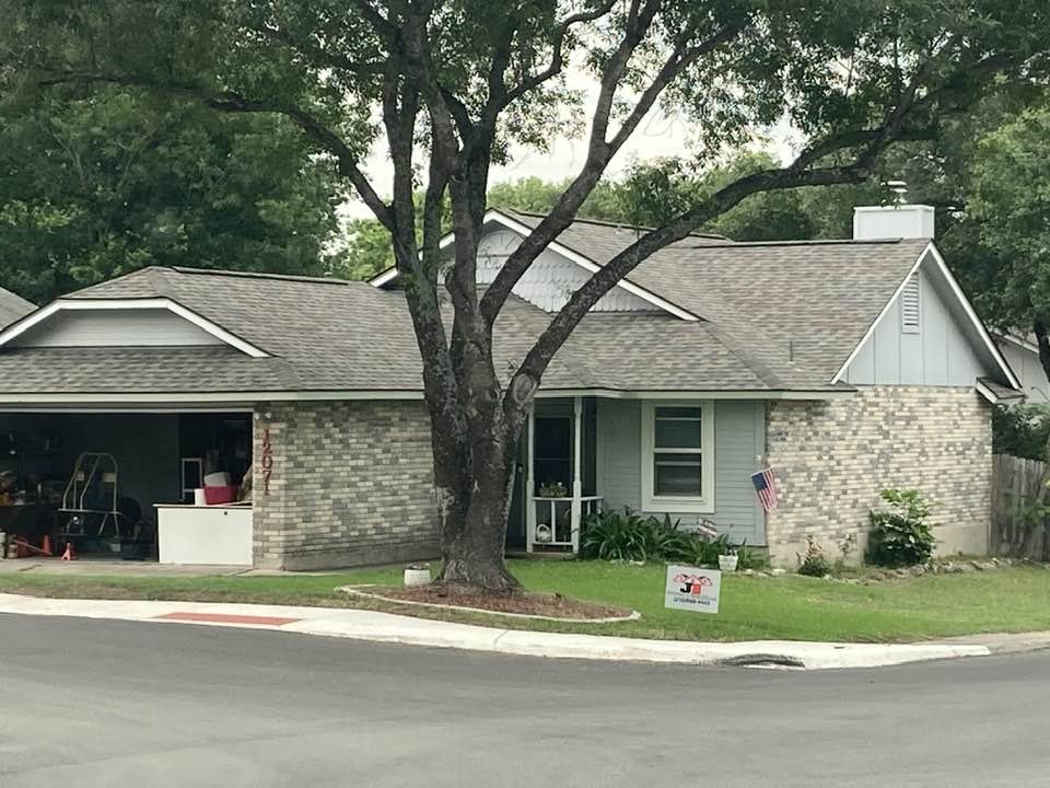 A house with a brick facade, a large tree in the front yard, and a sign promoting a landscaping company.