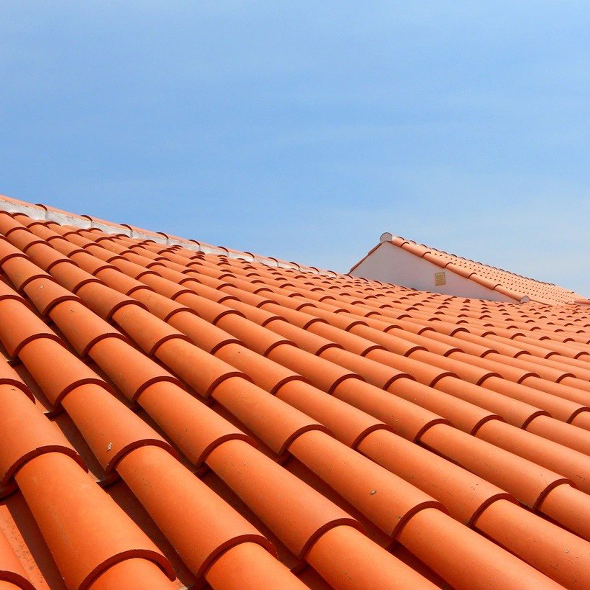 Close-up of orange clay roof tiles with a blue sky in the background.