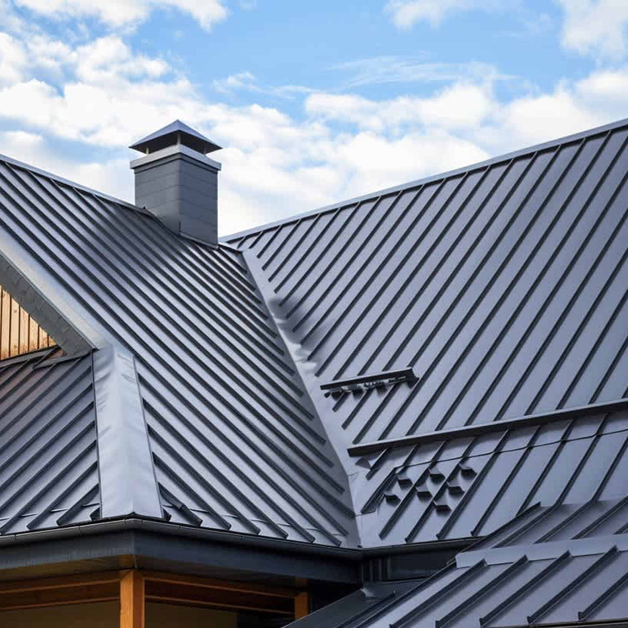Close-up of a modern metal roof with a chimney and vents under a partly cloudy sky.