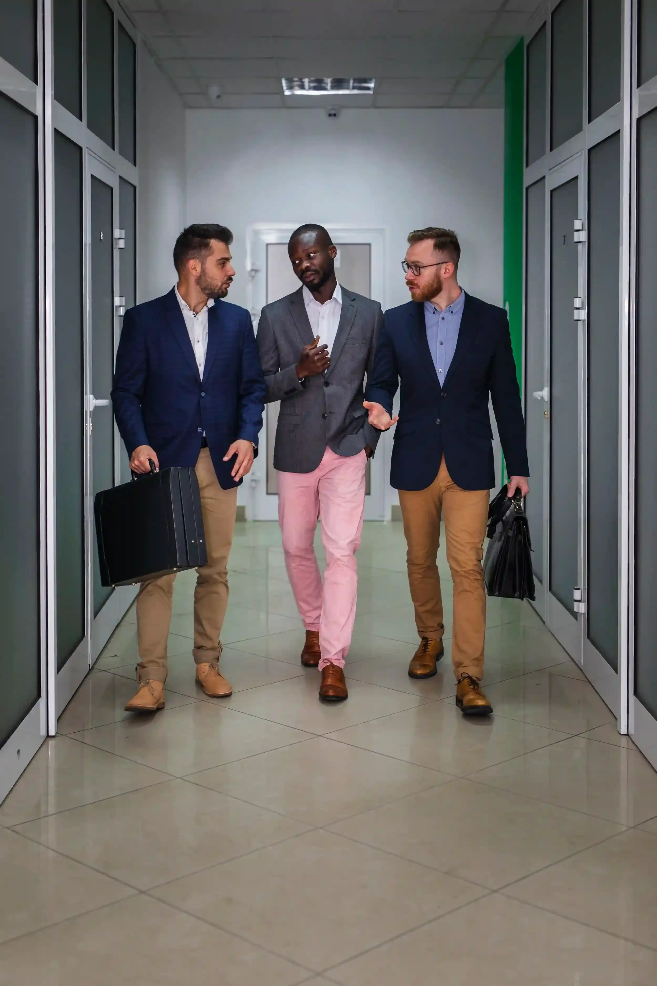 Three businessmen walking down a hallway, engaged in conversation. They are dressed in formal business attire and carrying briefcases.