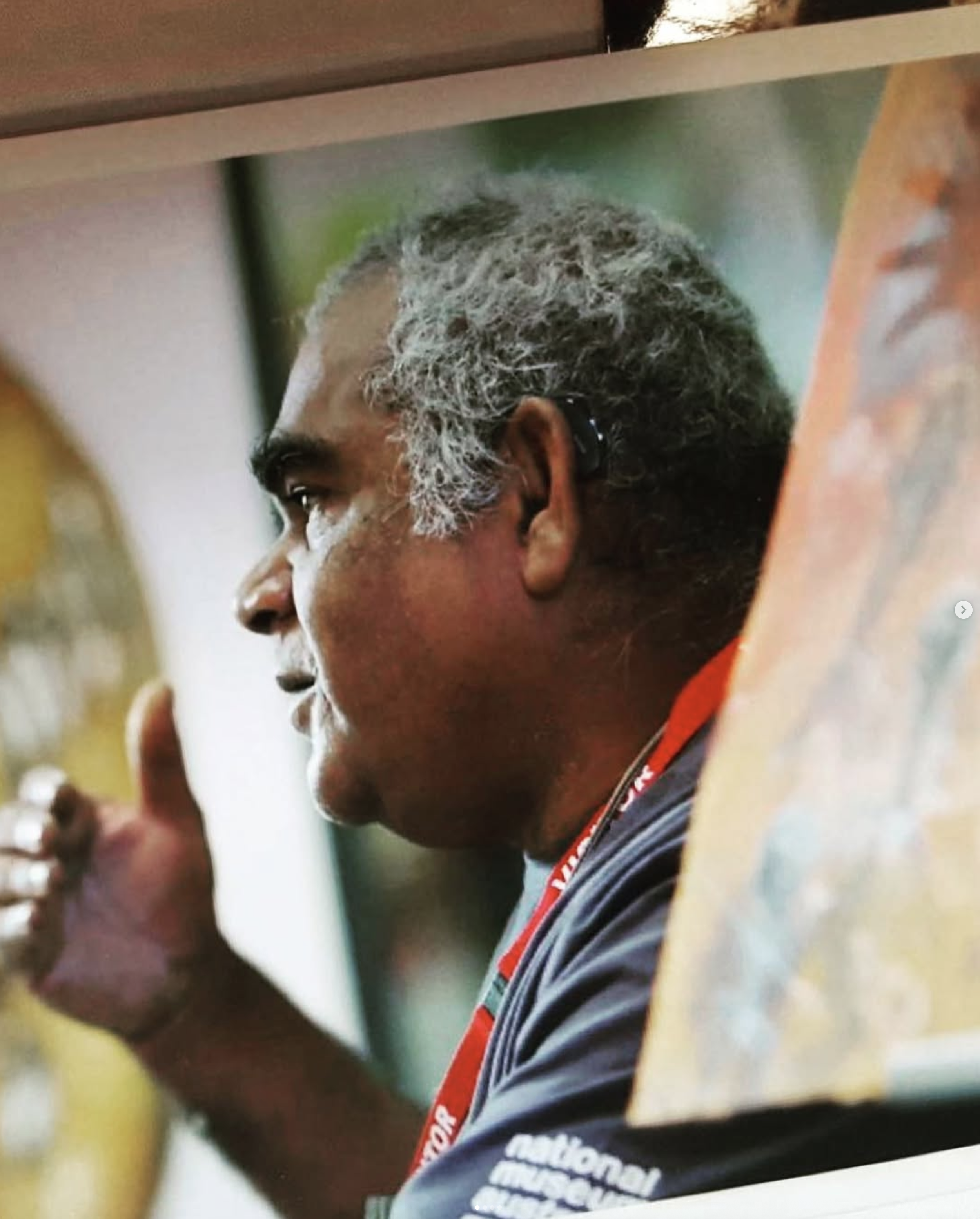 Paul Bong wearing a black shirt with white and red lanyards, sitting at a table, holding a glass, and engaged in a conversation.