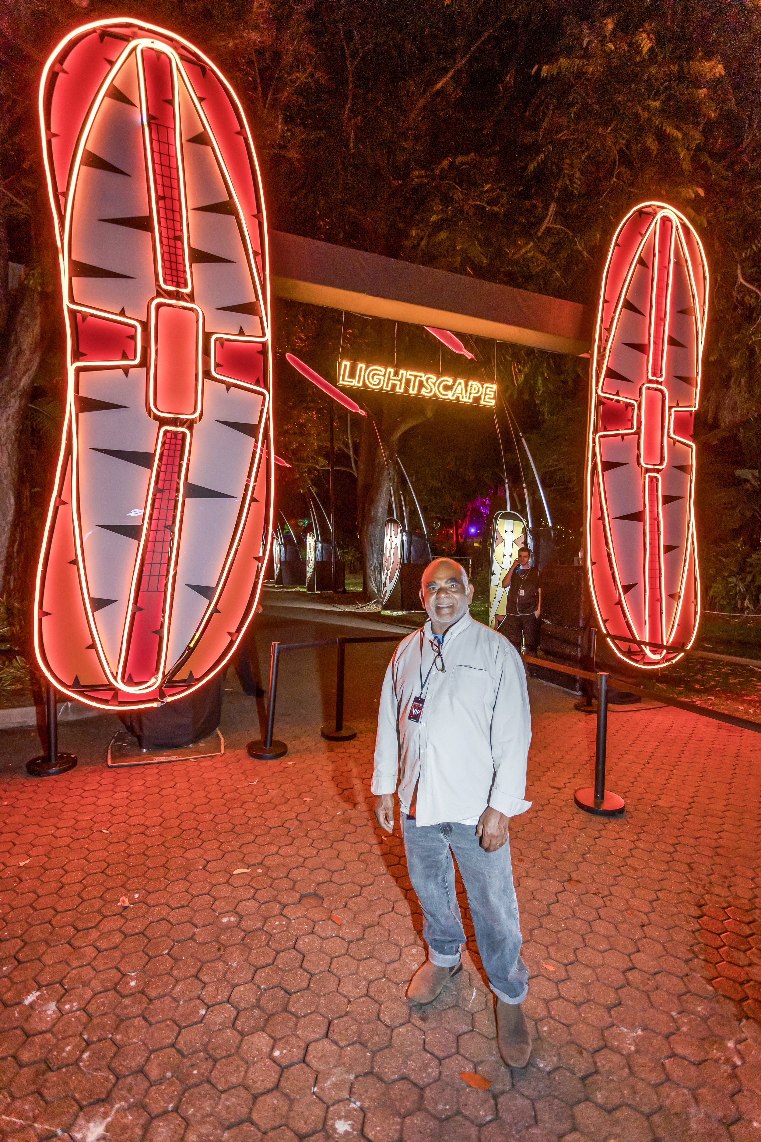 Paul standing in front of large Aboriginal shields at Lightscape event at night.