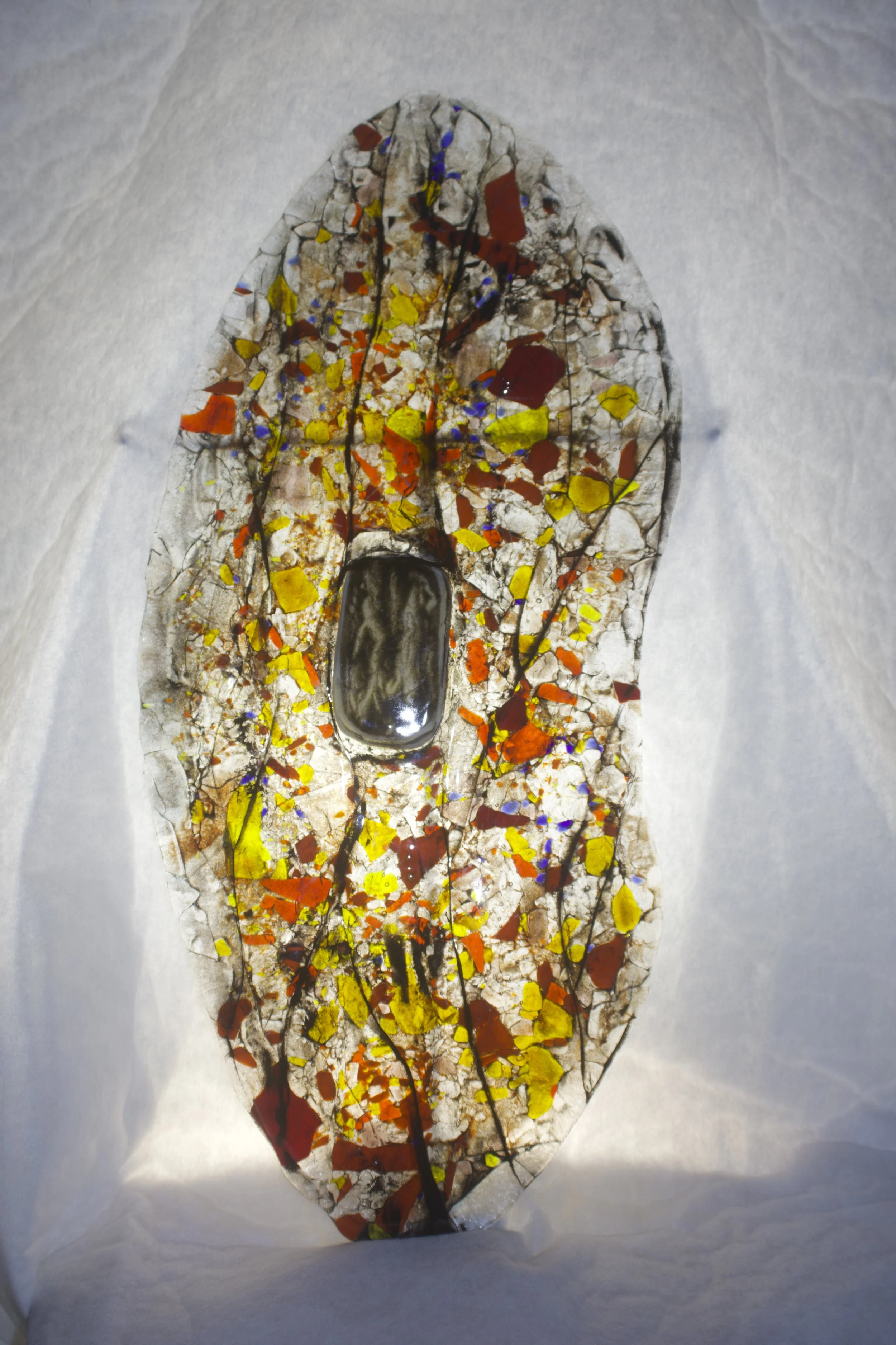 A decorative Aboriginal shield artwork, featuring a large brown oval in the center and a background with a cracked, colorful pattern featuring yellow, red, orange, and purple paint splashes on a white surface.