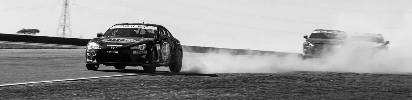 Black racing car leading a pack on a race track, kicking up dust behind as it overtakes others.