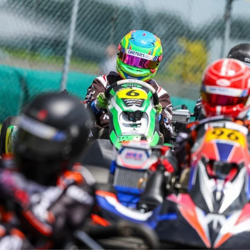 Motorcycle racers in colorful racing suits and helmets on a go-kart track.