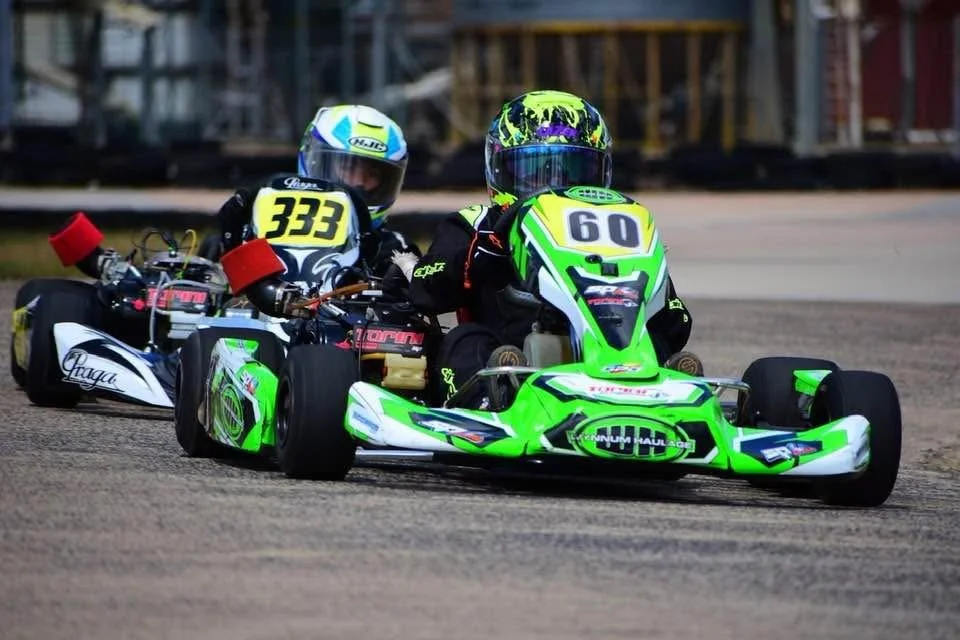 Two go-karts on a race track, with drivers wearing helmets and racing suits.