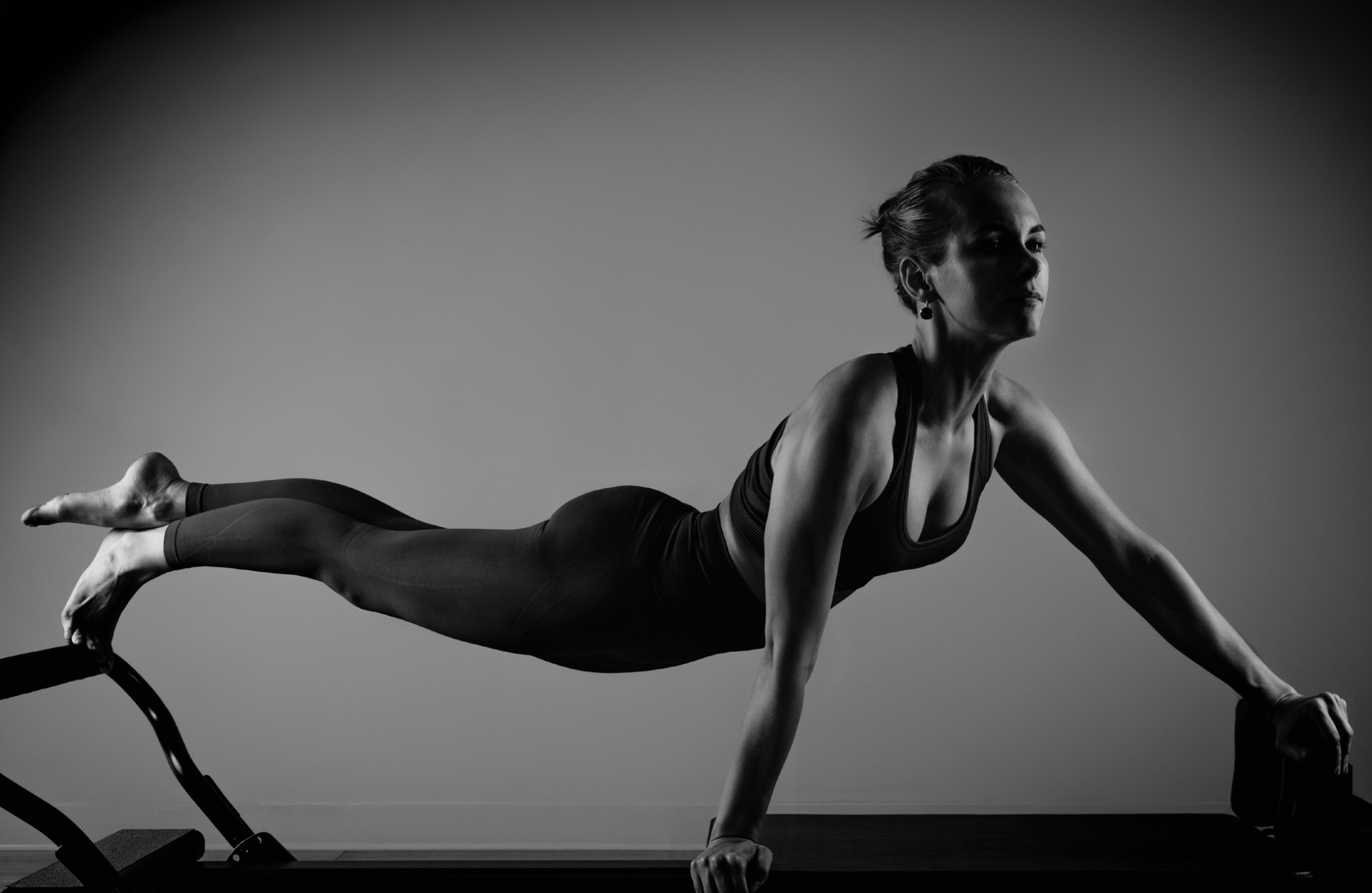 A woman in athletic clothing performing a plank exercise on a workout bench in a minimal setting.