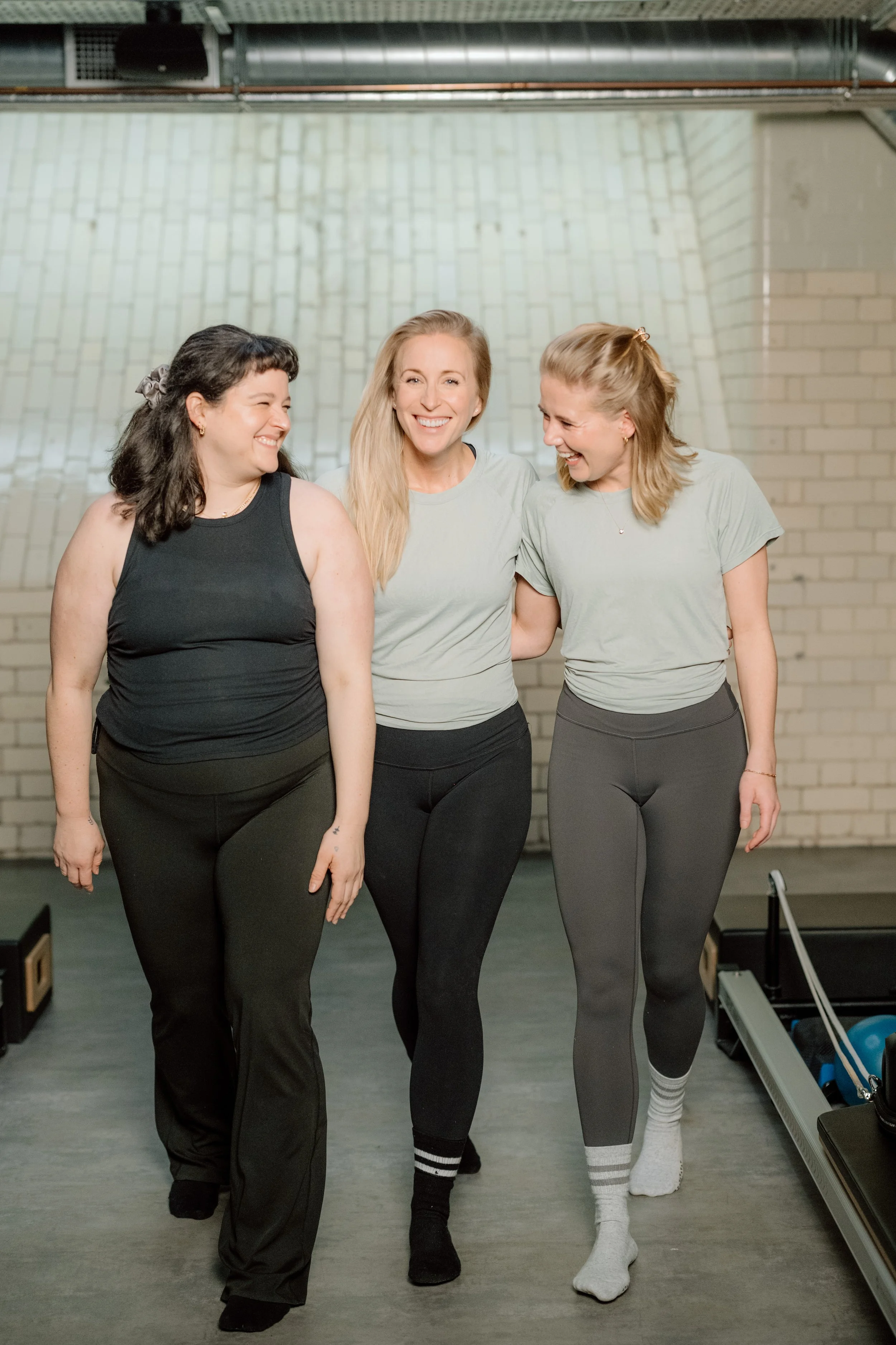 Three women smiling and walking together in a fitness studio, dressed in activewear.
