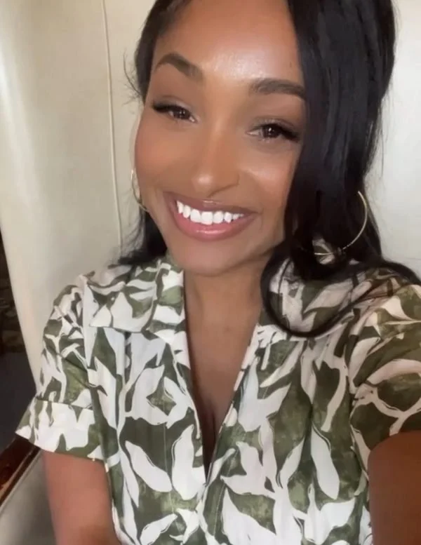 Smiling woman with dark hair, wearing hoop earrings and a leafy patterned blouse.