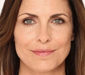 Close-up of a woman with brown hair and blue eyes, smiling softly.