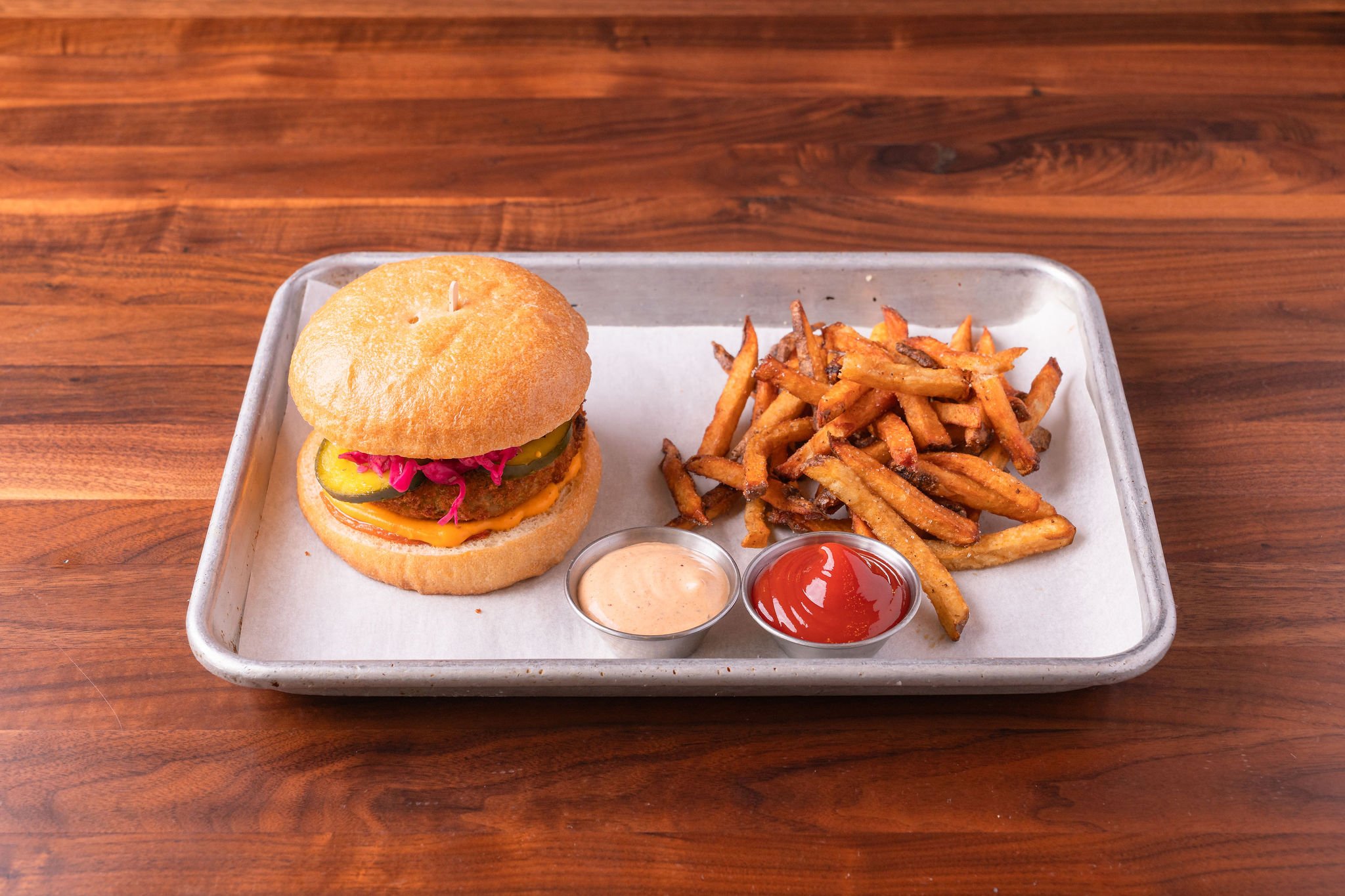 A tray with a burger, fries, ketchup, and a dipping sauce on a wooden table.