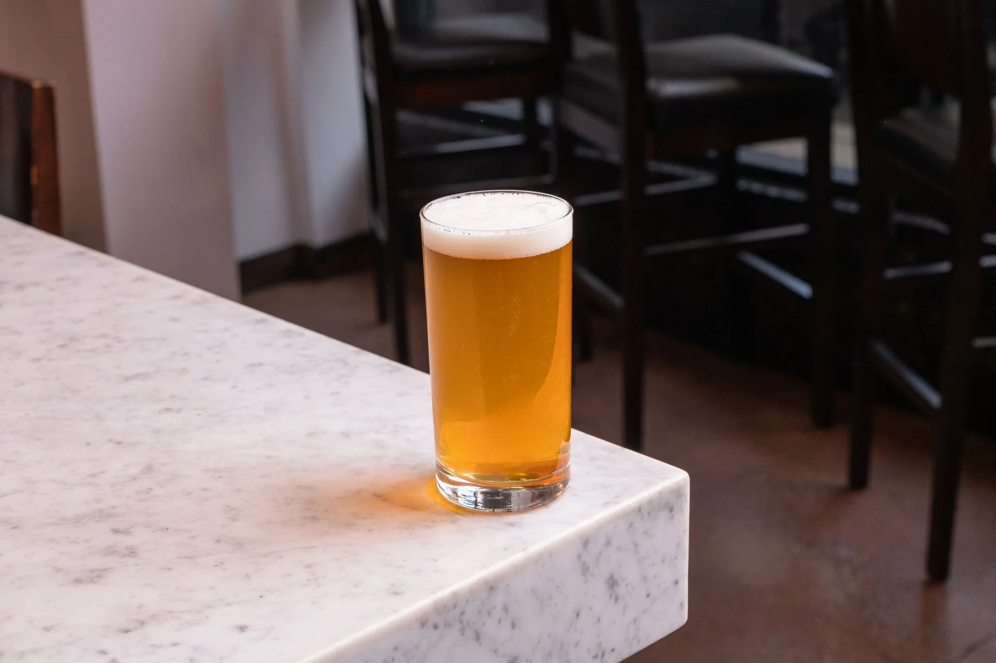 A tall glass of beer with a foamy head on a white marble bar counter.