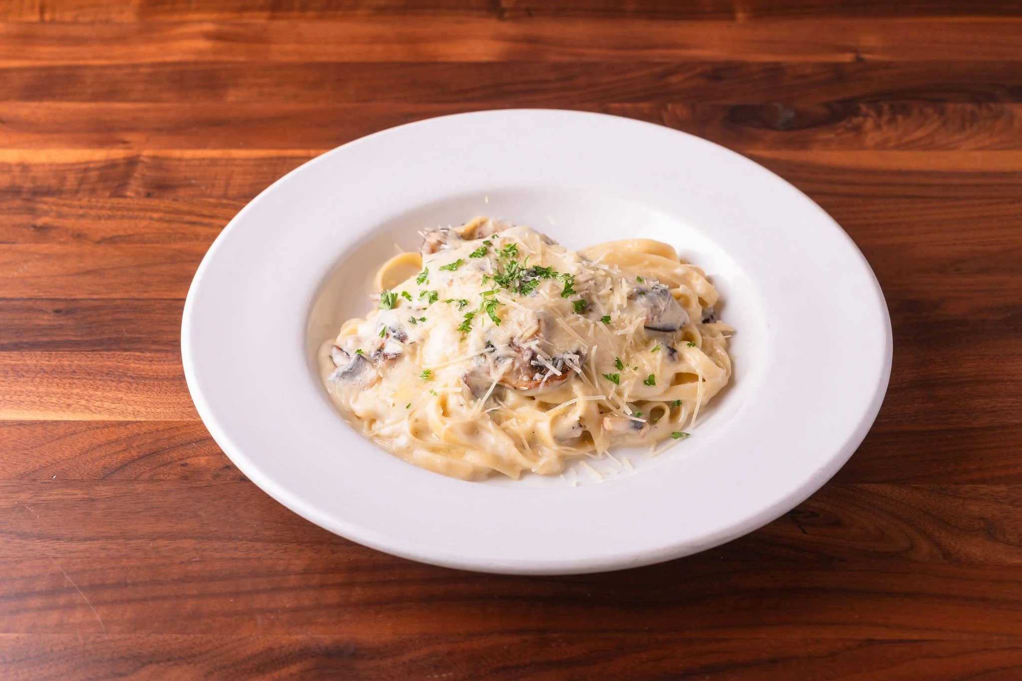 Plate of creamy fettuccine pasta with mushrooms, garnished with chopped parsley, on a wooden table.