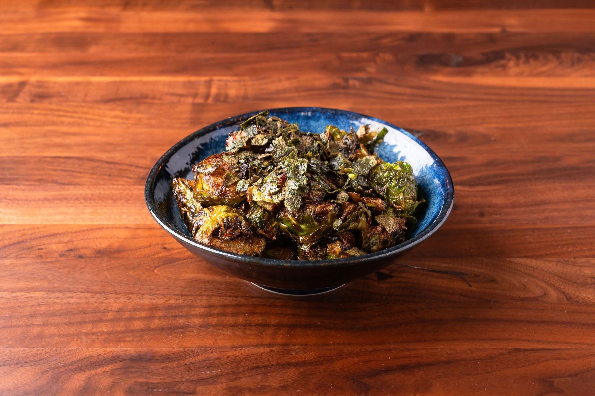 A black bowl filled with cooked Brussels sprouts and chopped herbs sitting on a wooden table.