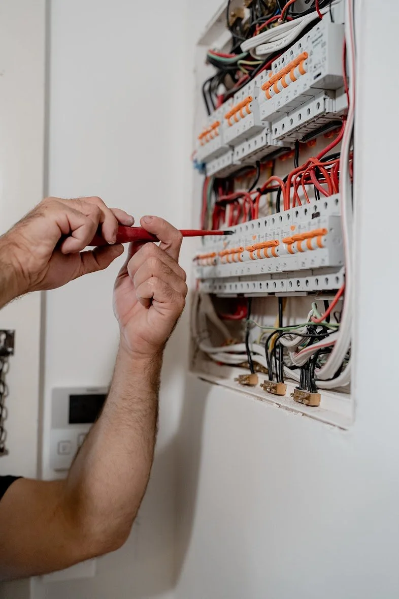A person working on an electrical panel with various wires and circuit breakers.